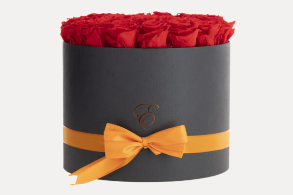 Caja redonda negra de lujo con vibrantes rosas rojas preservadas, adornada con un lazo naranja, ideal para regalar y decorar.